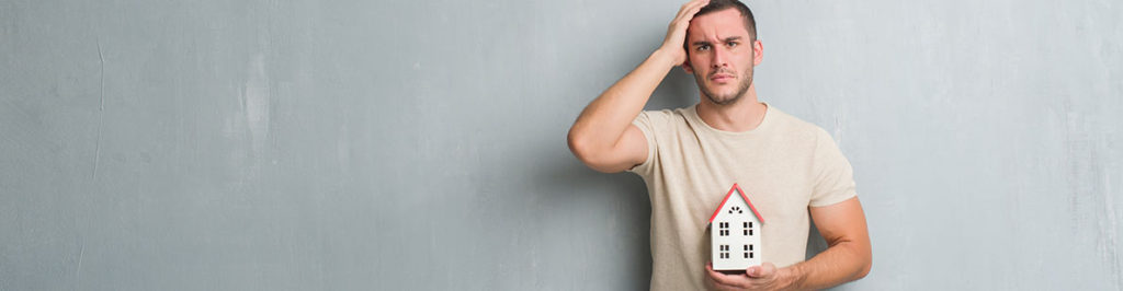 Nachdenklicher Mann mit Miniaturhaus in der Hand