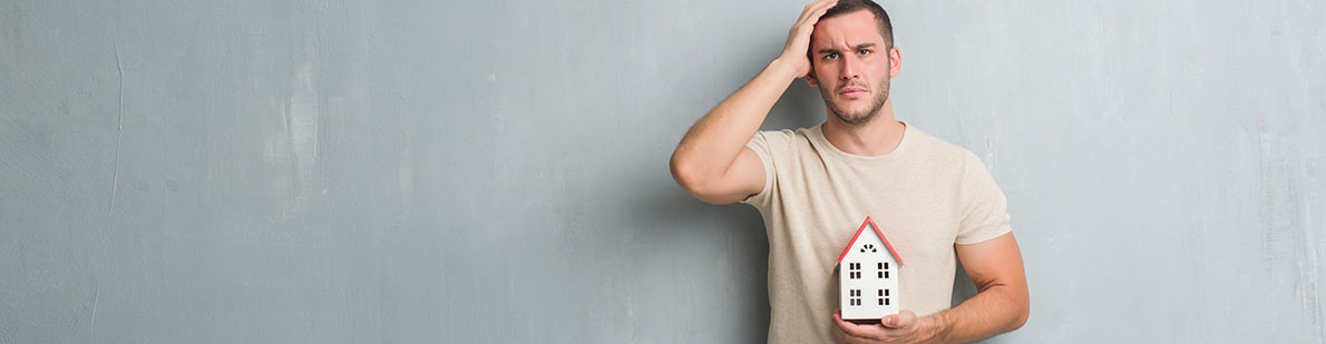Nachdenklicher Mann mit Miniaturhaus in der Hand
